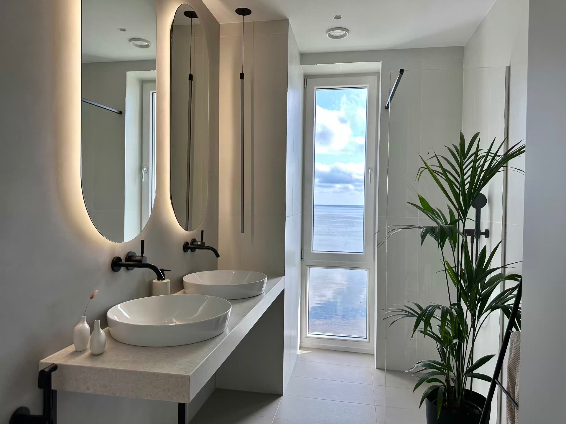 The bathroom with two basins, backlit mirrors and a window to the sea