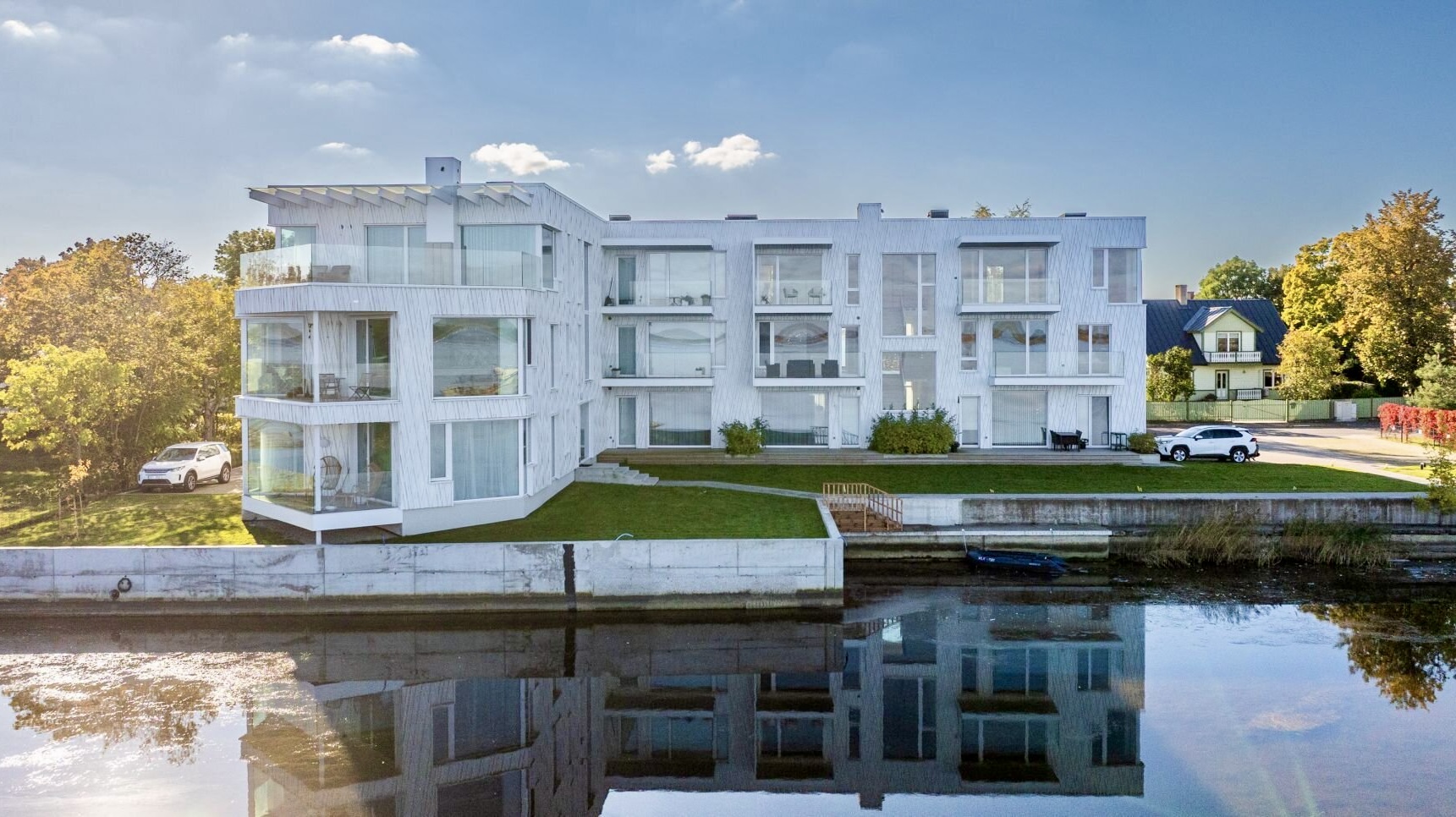 The white Sadama 26 building in Haapsalu seen across the water, parking in front
